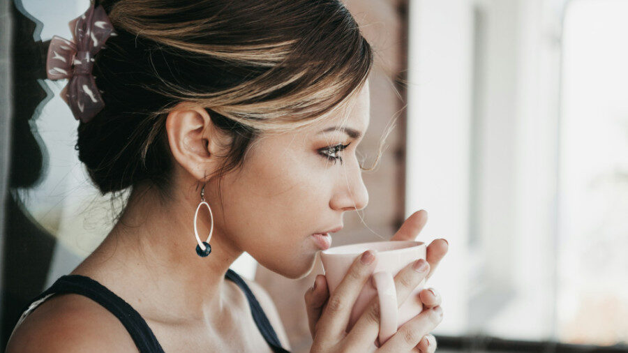 Young woman drinking from a white cup, wearing a hair clip and earrings.