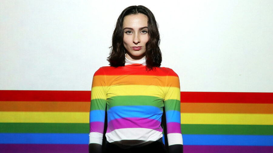 Woman wearing a rainbow-striped shirt standing in front of a rainbow-striped background.