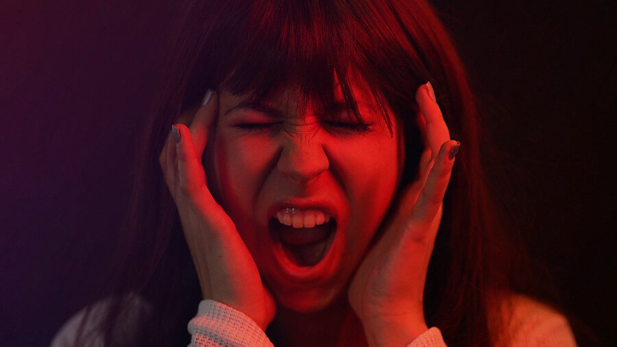 Woman screaming with her hands on her head, illuminated by red light.