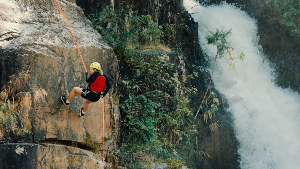 Person rappelling down a cliff near a waterfall.