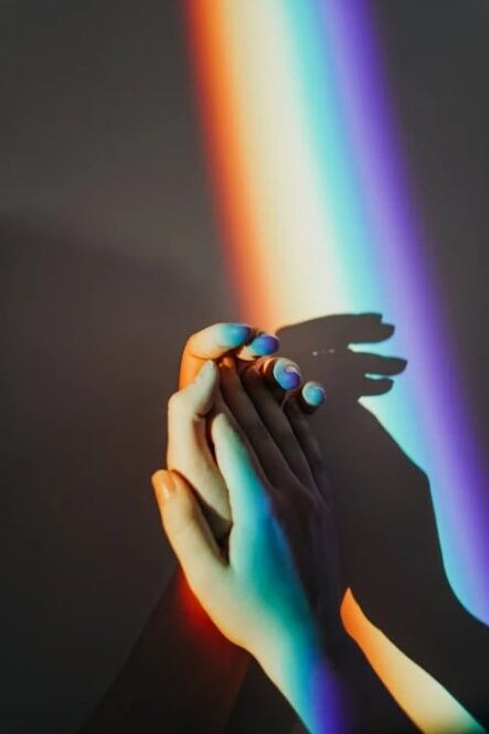 Hands touching under a rainbow light, casting a colorful shadow.