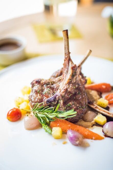 Plate of lamb chops served with vegetables and garnished with rosemary.