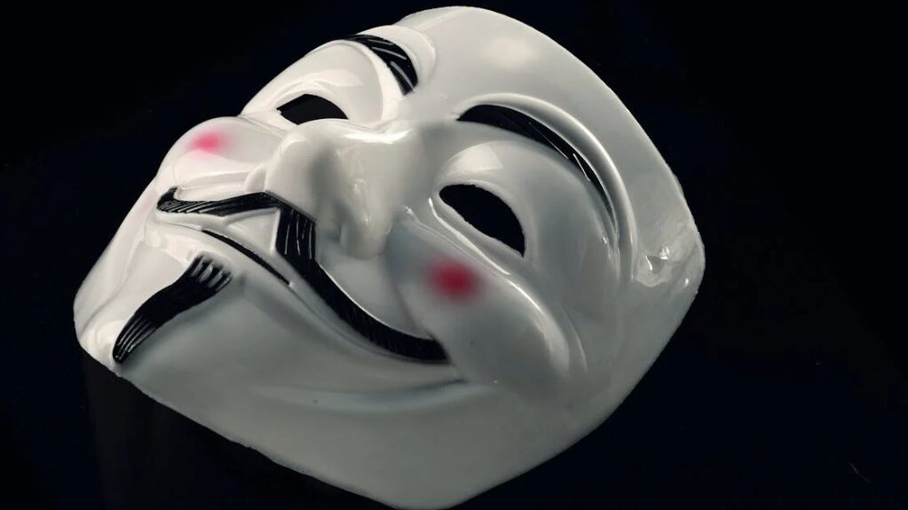 Close-up of a white Guy Fawkes mask lying on a dark surface.