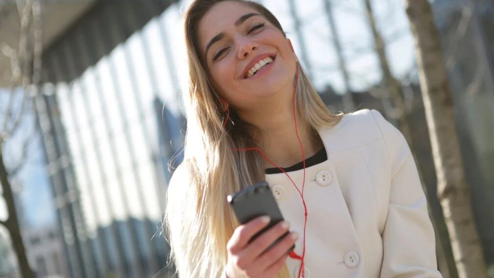 Woman smiling while listening to music with earphones and holding a smartphone.