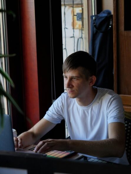 Man using a laptop near a window, with sunlight coming through.