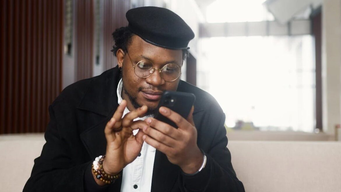 Man wearing glasses and a beret using a smartphone indoors.