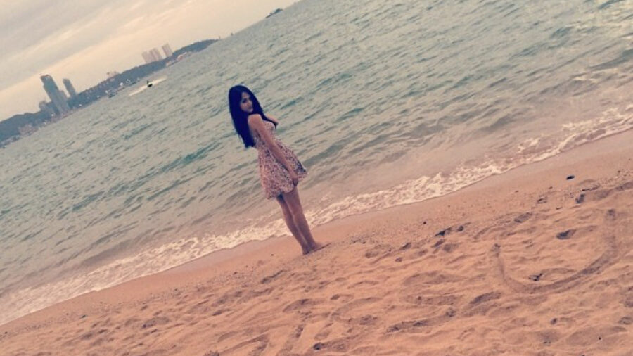 Nguyen Huong Giang standing on a beach, with a calm sea and cityscape in the background. Image from Instagram @huoggiangggg