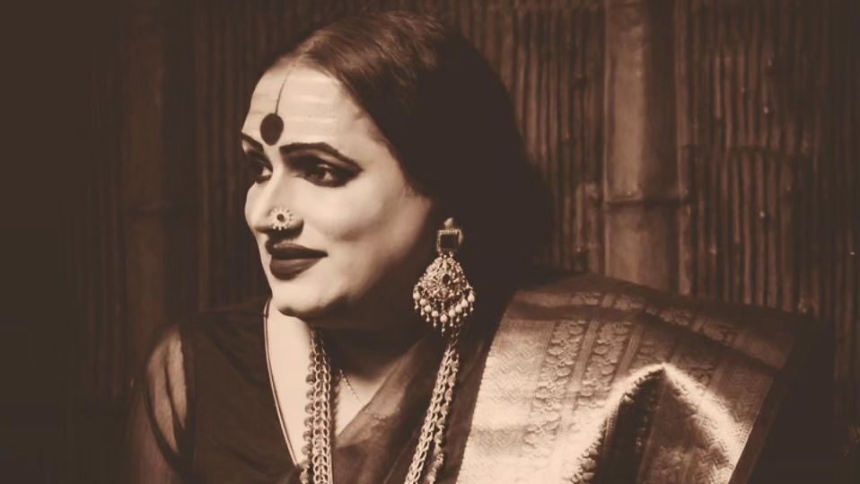 Sepia-toned image of Laxmi Narayan Tripathi, wearing traditional Indian jewelry, including a nose ring and large earrings, draped in a sari, gazing off to the side. Image from Instagram @aa_mediaprojects.