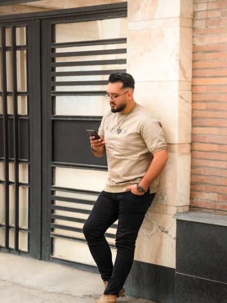 Man leaning against a wall outdoors, looking at his smartphone.