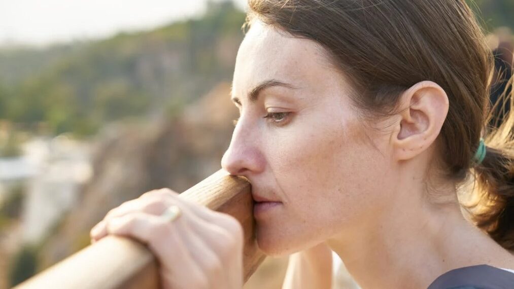 Side profile of a woman leaning on a railing, appearing deep in thought.