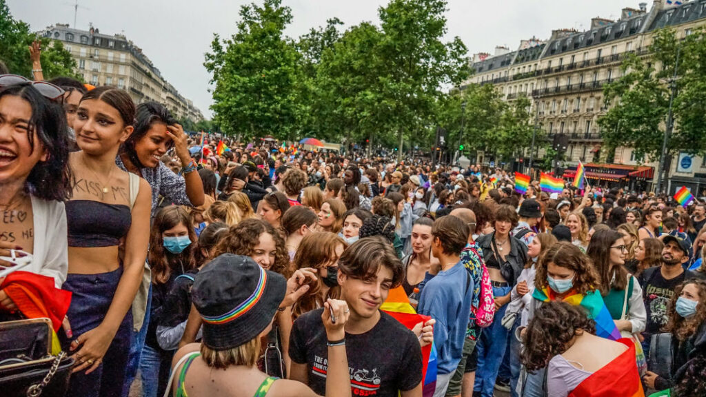 People gather at a pride parade, celebrating unity and support for the LGBTQ+ community with rainbow flags.