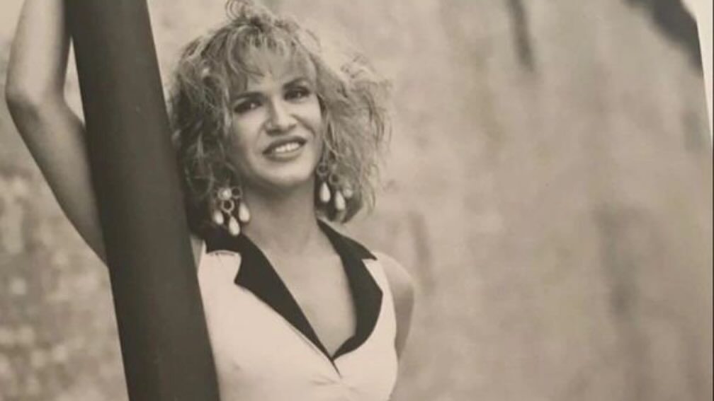 Cristina Ortiz Rodríguez, wearing a white dress and statement earrings, poses confidently in a black-and-white photograph.