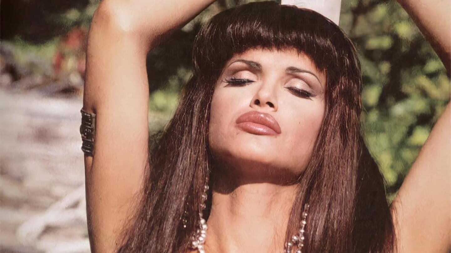 Cristina Ortiz Rodríguez poses with her arms raised, wearing a bikini top and a long necklace, eyes closed in a serene outdoor setting.