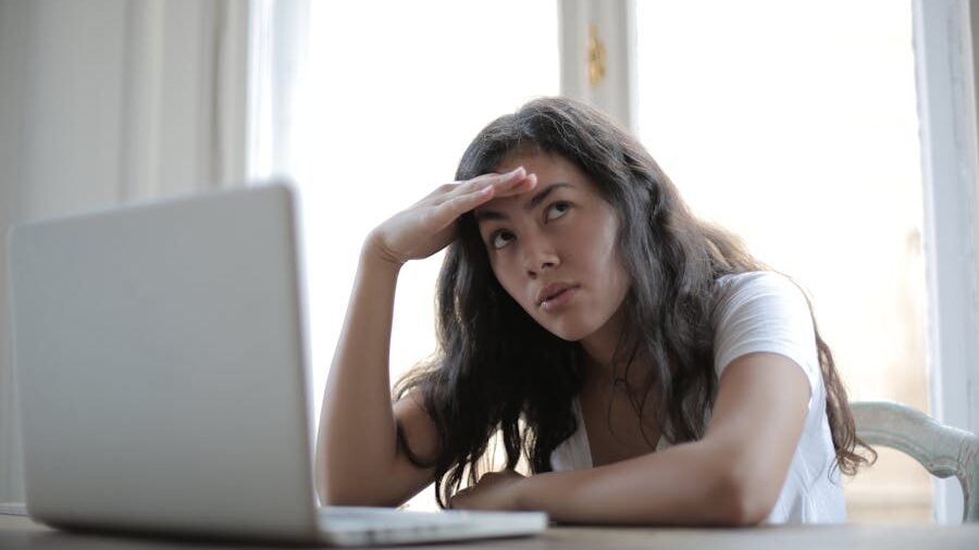 Woman sitting at a desk with a laptop, looking frustrated with her hand on her forehead.