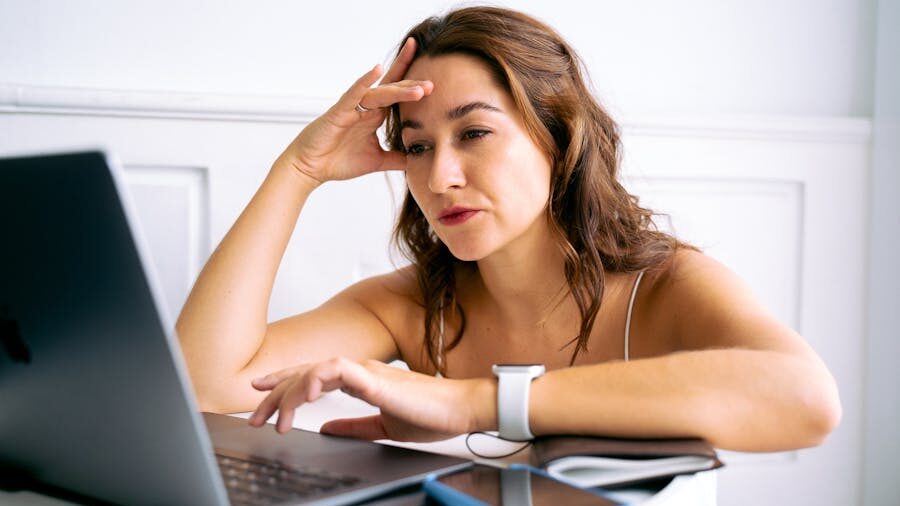 Woman sitting at a desk, looking at her laptop with a pensive expression.