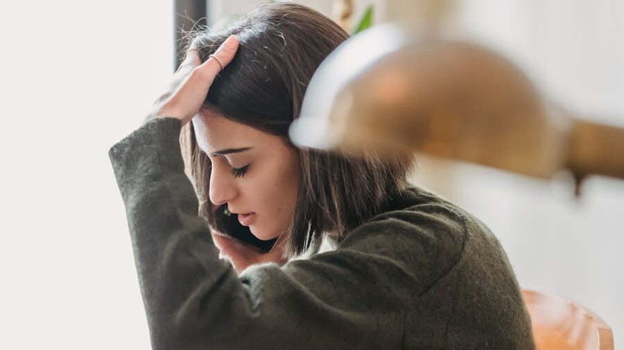 Woman talking on the phone, resting her hand on her head, appearing stressed.