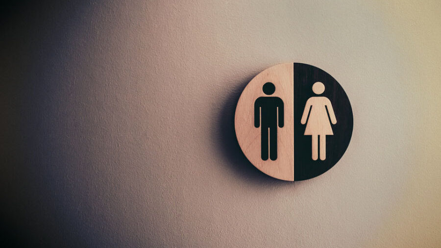 A wooden restroom sign split between male and female symbols, representing binary gender.