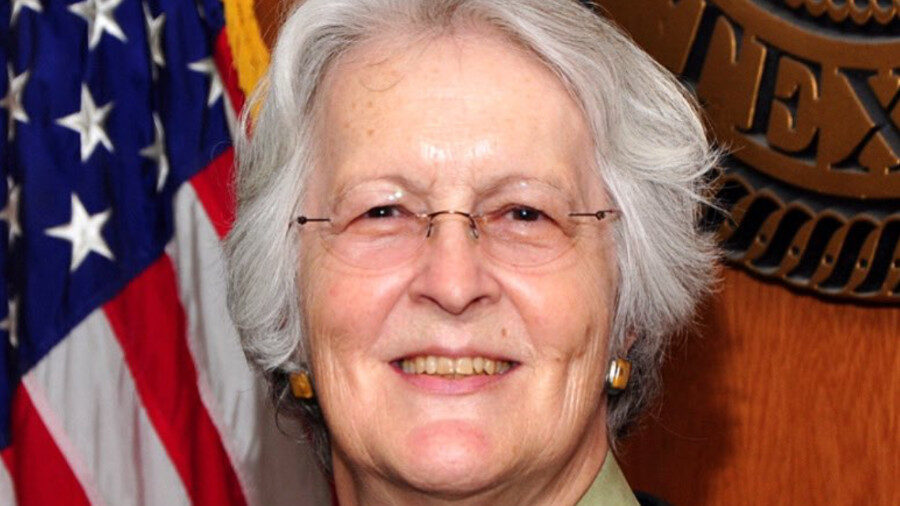 Phyllis Frye, wearing a judge's robe, standing in front of the American flag and the Texas state seal.