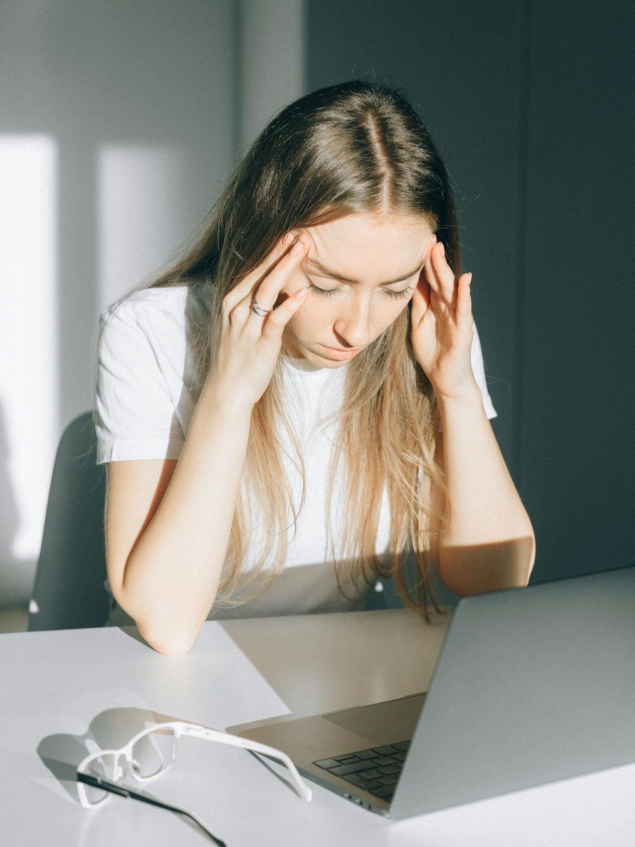 Woman at a desk, appearing stressed or overwhelmed, with her hands on her temples.