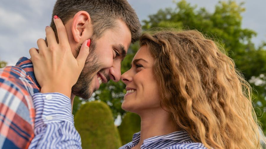 A couple embracing affectionately, their foreheads almost touching, with greenery in the background.