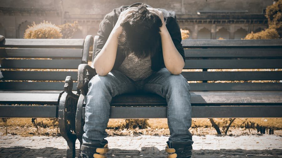 Person sitting alone on a bench, bent forward with their hands on their head, in a moment of despair.