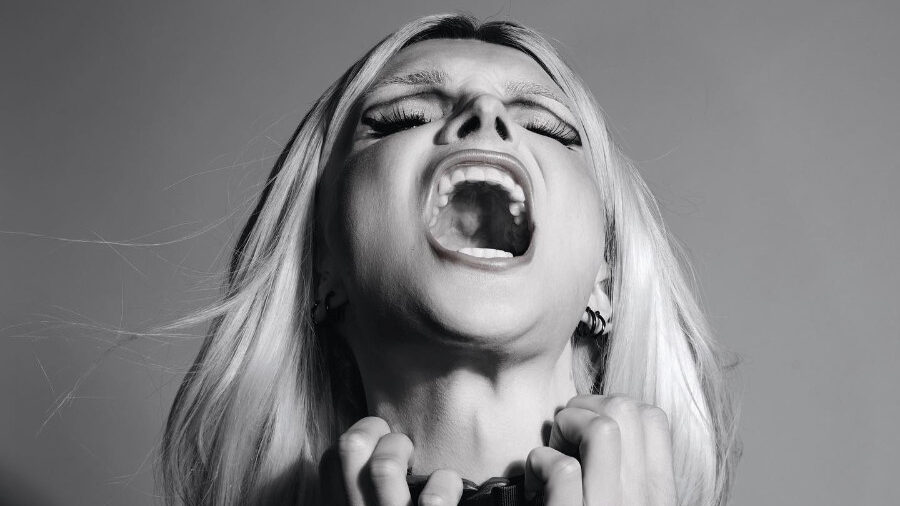 Black-and-white close-up of Dylan Mulvaney with mouth open and hands clenched, expressing intense emotion.