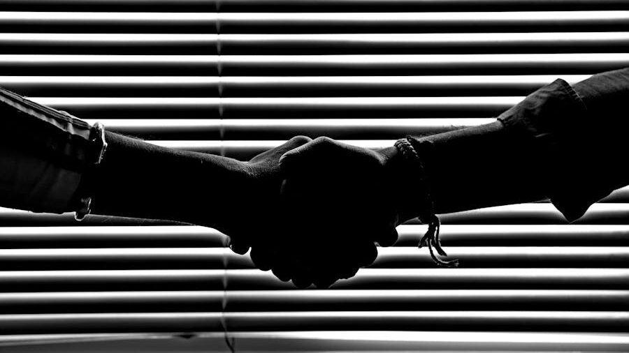 Silhouette of two hands shaking in front of window blinds, creating a striped shadow effect.