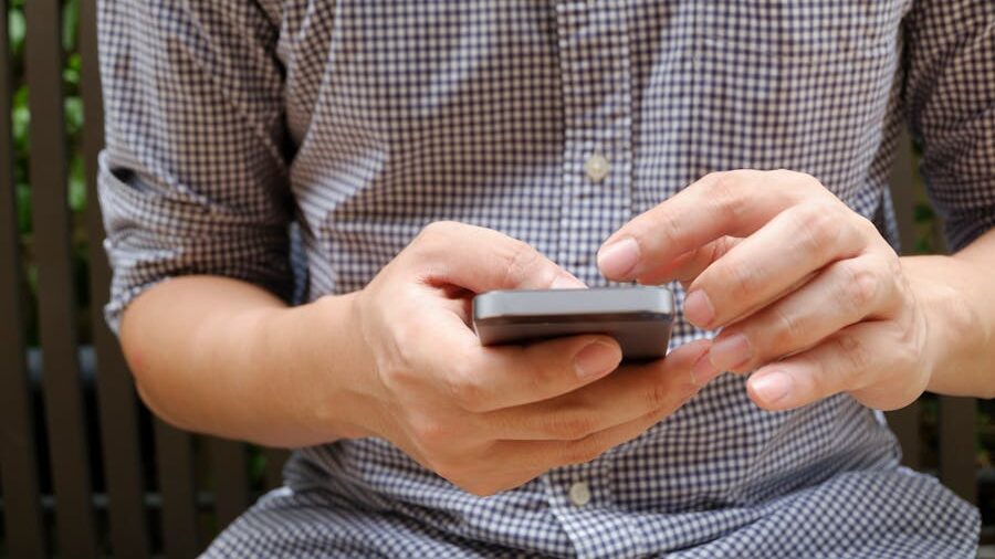 Person in casual attire typing on a smartphone while seated.