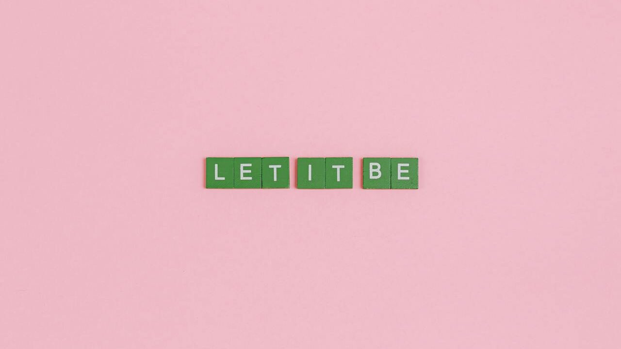 Green letter tiles spelling "LET IT BE" on a pink background.