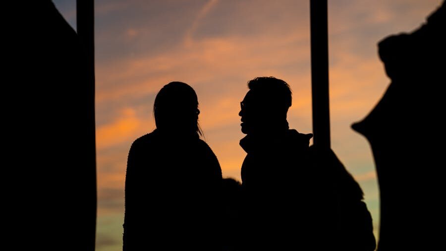 Silhouette of two people talking against a sunset sky.