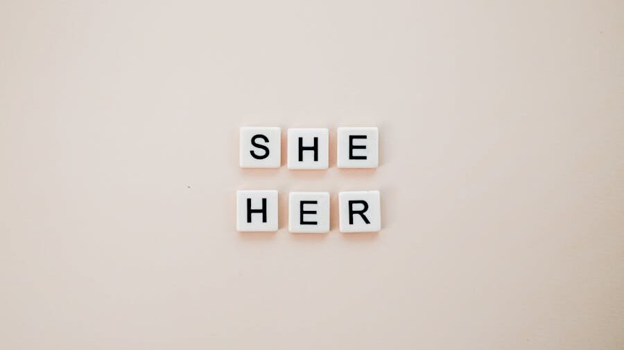 Scrabble-style tiles spelling "SHE" and "HER" on a plain beige background.