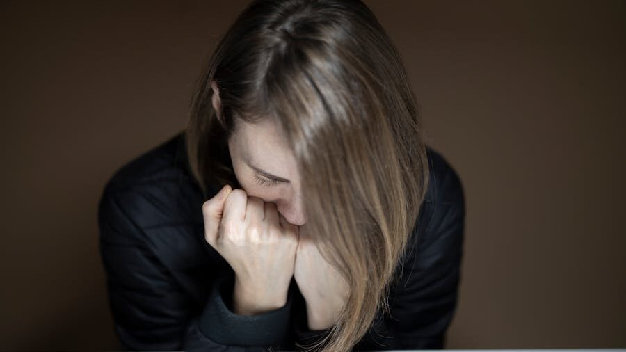 A woman with her head bowed, resting her chin on her clenched hands, appearing reflective or distressed.