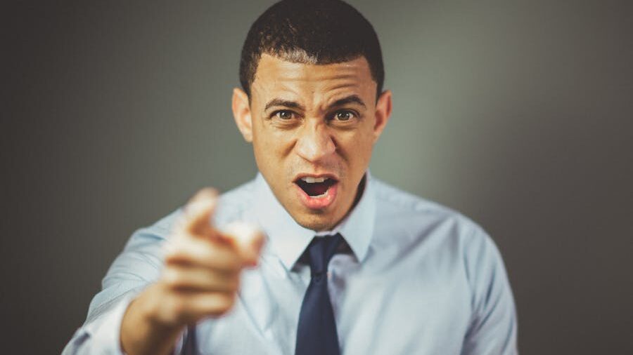 A man in a shirt and tie pointing directly at the camera with a stern and intense expression.