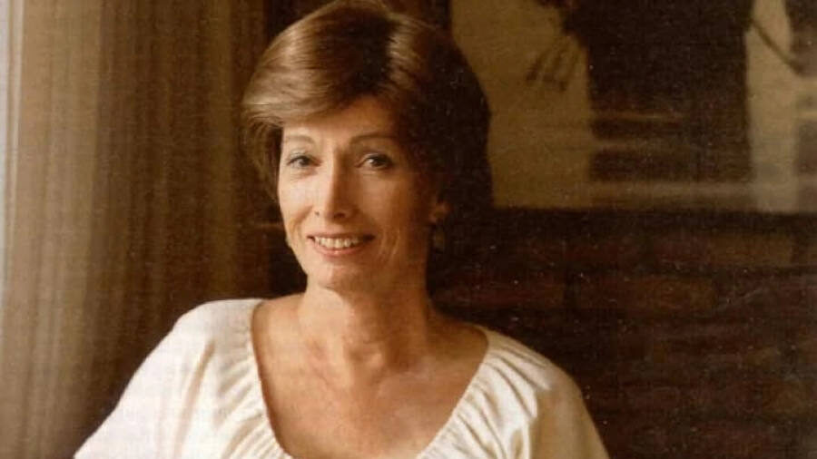 Lynn Ann Conway smiling while seated, wearing a white blouse, in a warmly lit room with a neutral background.