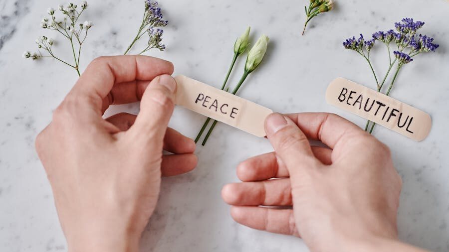 Two hands holding strips of paper with the words "PEACE" and "BEAUTIFUL," placed on a marble surface with small flowers in the background.