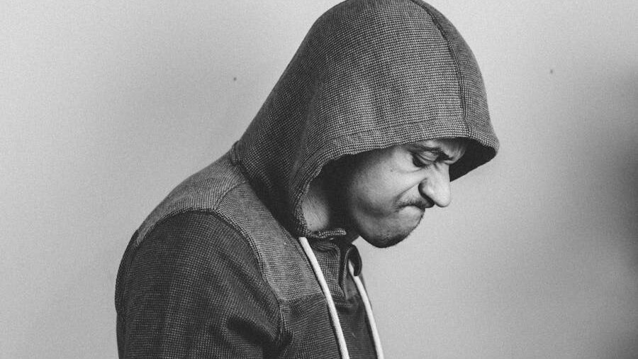 Monochrome portrait of a man in a hoodie, showing a tense expression as he looks downward.