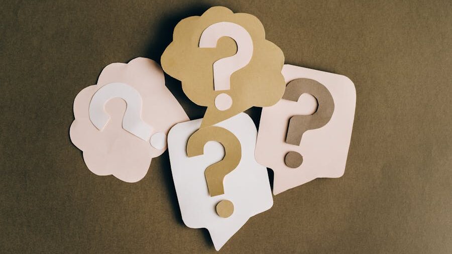 Multiple paper cut-outs of question marks in varying shapes and neutral tones on a brown surface.