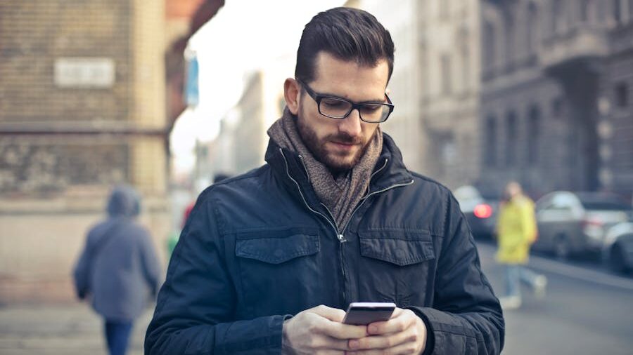 Person dressed warmly, engrossed in their phone, walking on a busy city street.