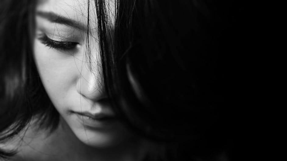 Black-and-white close-up of a woman’s face, partially covered by her dark hair, with a serene expression.