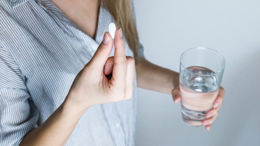 Hand holding a pill while the other holds a glass of water, ready for consumption.