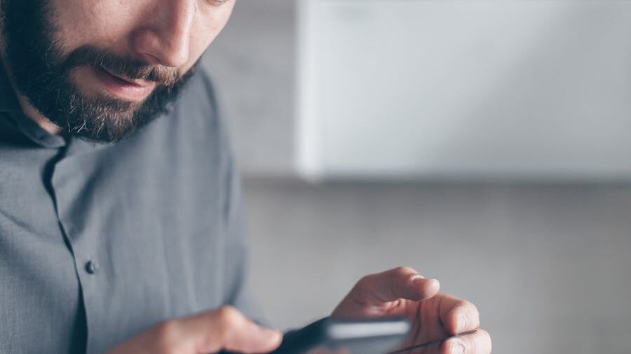 A man scrolling on his smartphone, appearing deep in thought or concerned about something he’s reading.