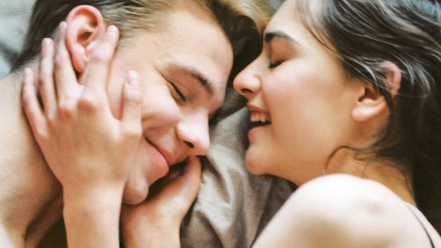 A young couple lying close together, smiling as they share an intimate moment.