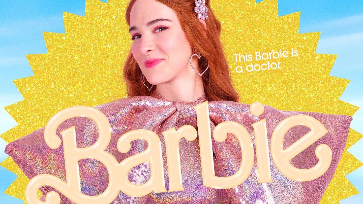 Promotional poster of Hari Nef as Doctor Barbie in the Barbie (2023) movie. She wears a sparkling pink dress with dramatic shoulder details, standing against a bright yellow and blue background.