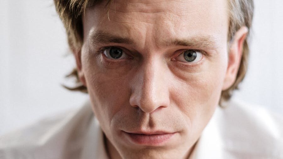 Focused expression of a man in a white shirt, with a neutral background.