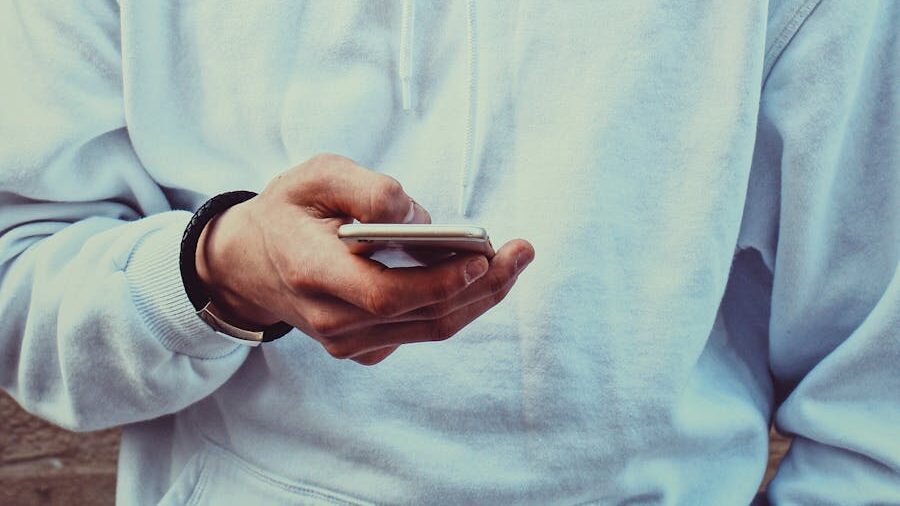 Focused shot of a hand holding a smartphone, with a white hoodie in the background.