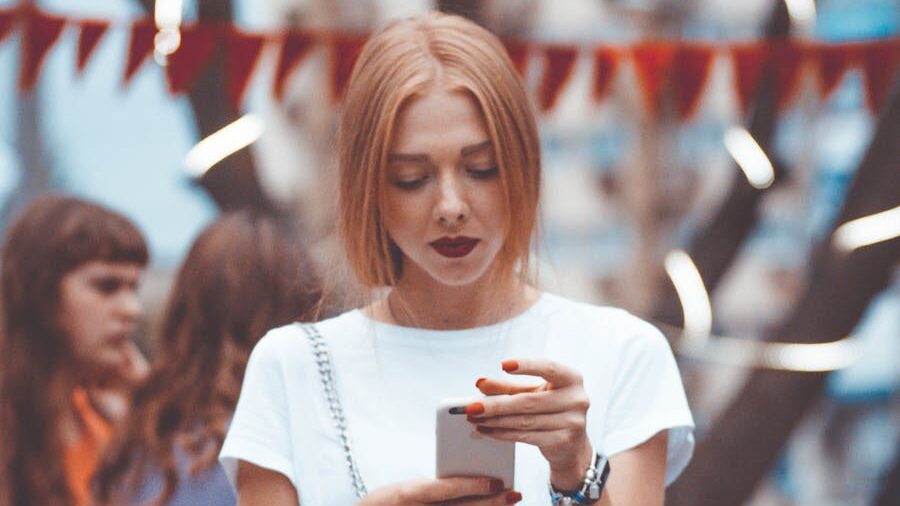 Young woman with red hair looking at her smartphone during an outdoor event, red flags in the background.