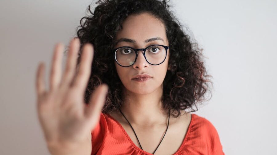 Person holding up hand in a stop gesture, wearing glasses and a red top.