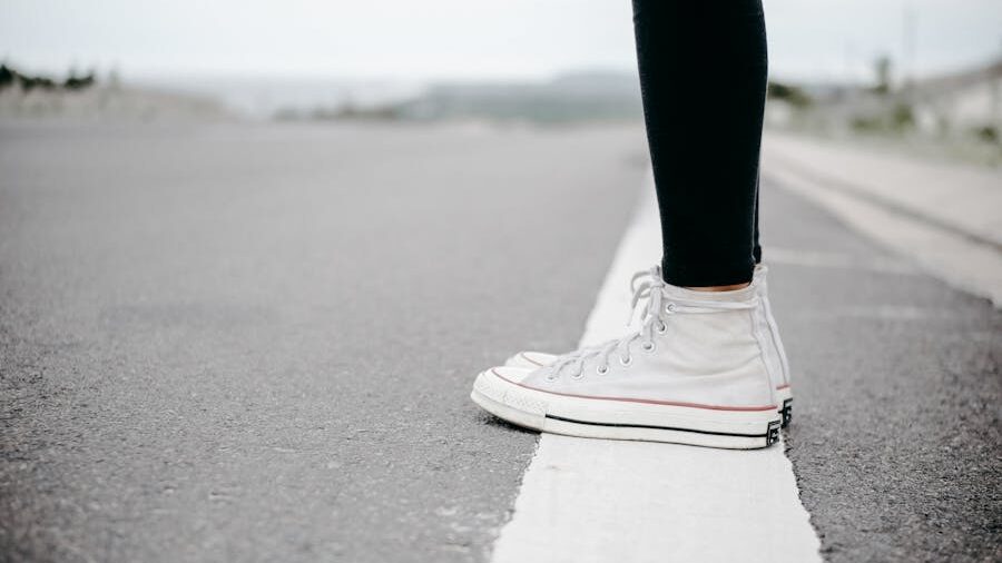 Close-up of a person in white high-top sneakers standing at the edge of a painted line on an empty road, symbolizing a moment of decision or boundary.