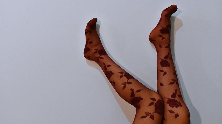 A pair of legs wearing sheer floral-patterned tights raised against a blank wall, highlighting sensuality while inviting reflection on objectification and fetishization.