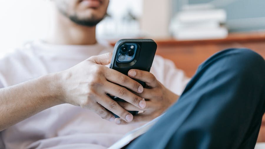 Close-up of a man sitting down, holding a smartphone with both hands and looking at the screen, his face partially out of frame.